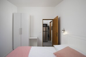 A bedroom with a bed, a wardrobe, a bedside table, and a door leading to a kitchen area. - Apartment SoMi 3 (Poreč)