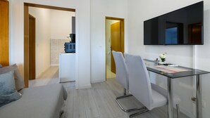 Moderni hotellihuone, jossa on sänky, työpöytä tuolilla, taulutelevisio ja pieni keittonurkkaus.