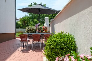 Une terrasse extérieure avec une table et des chaises, un grand parasol et un barbecue.