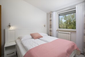 A bedroom with a bed, a nightstand, a radiator, and a window with curtains.