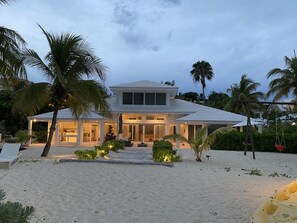 Une propriété située en bord de mer, comprenant une grande maison, des palmiers et une plage de sable.
