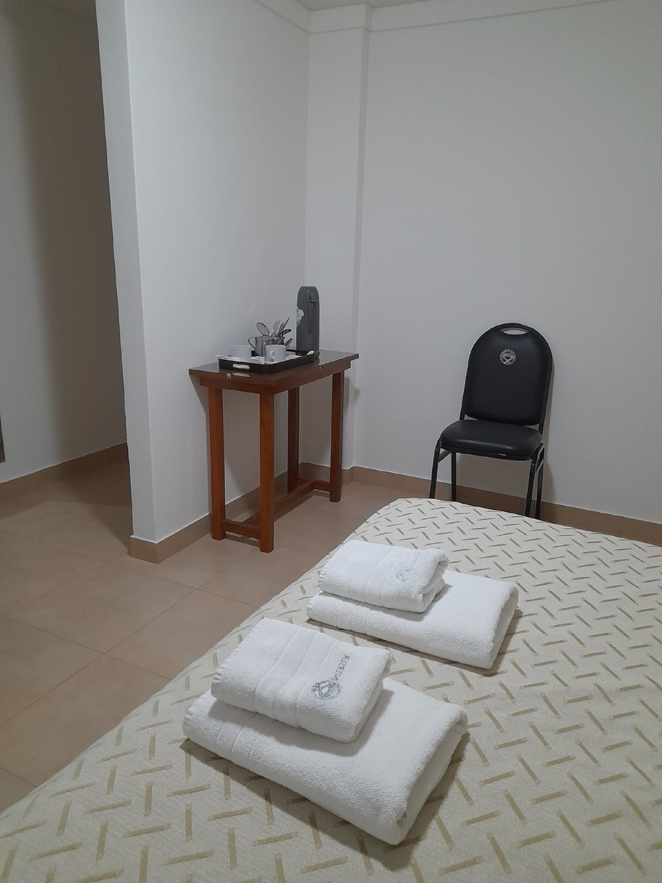 A hotel room with a bed, a small wooden table with a tray of toiletries, and a black chair.