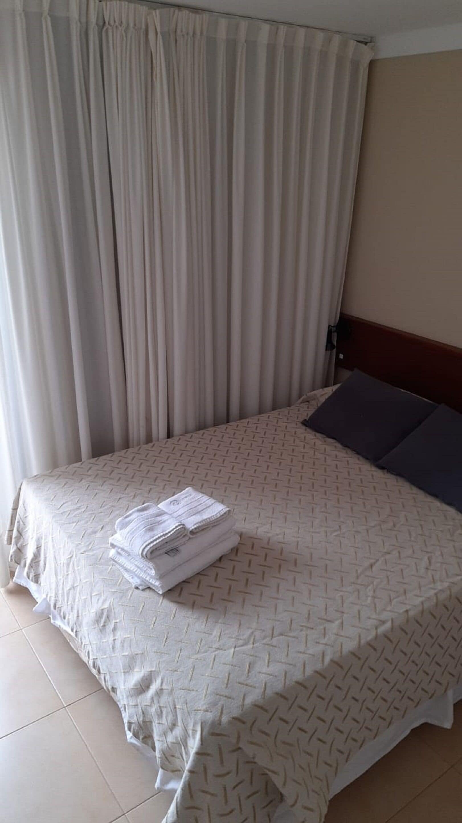 Uma cama bem arrumada com um cobre-leito estampado, uma toalha dobrada e um travesseiro escuro.