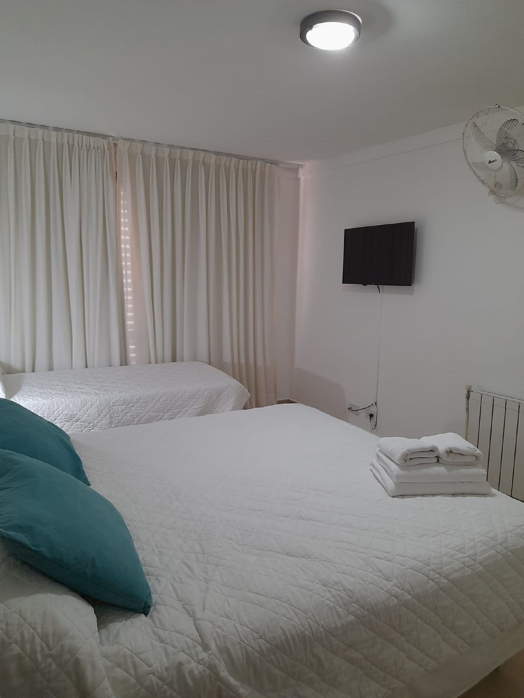 Une chambre d’hôtel avec deux lits, un téléviseur à écran plat, un ventilateur de plafond et un radiateur.