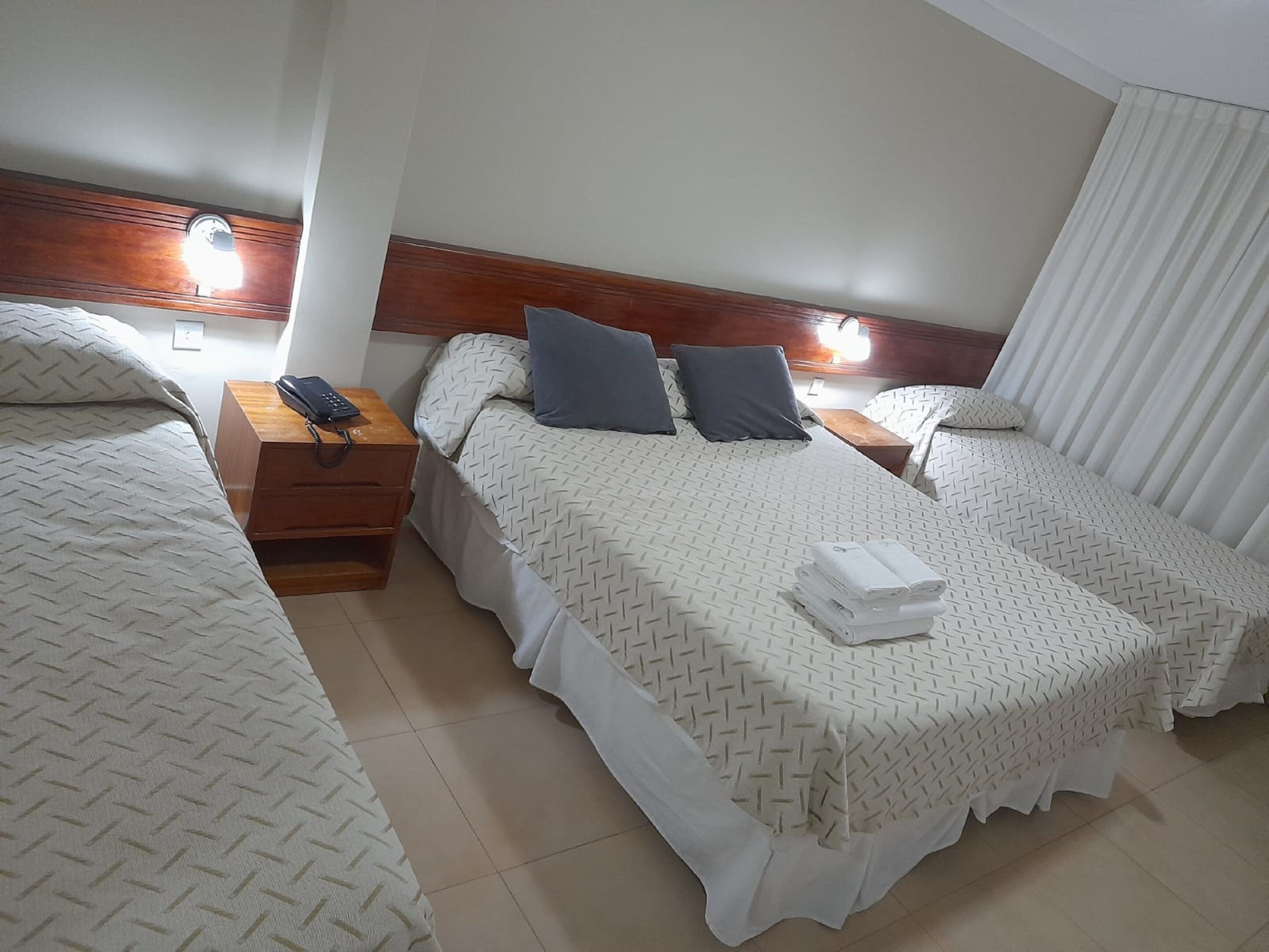 A hotel room with two beds, each with a wooden headboard, white bedding, and a nightstand with a telephone.