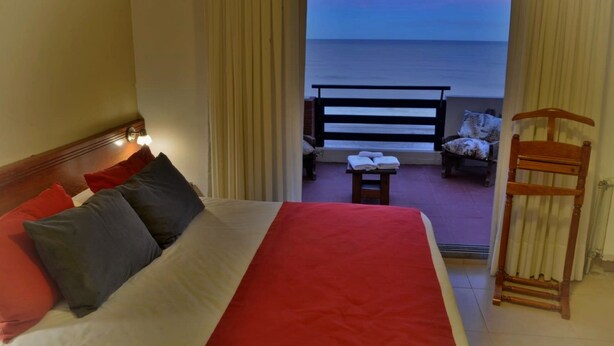 A hotel room with a bed, a view of the ocean, a balcony with a chair and a table, and a radiator. - Intersur Villa Gesell (Villa Gesell)