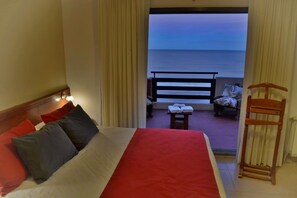 Quarto de hotel com cama, vista para o oceano, varanda com cadeira e mesa, e radiador.