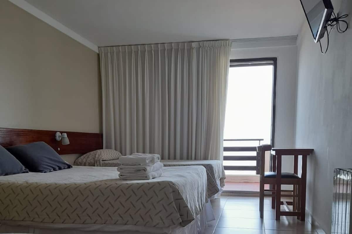 A hotel room with two beds, a desk, and a large window.