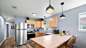 Una cocina moderna con una isla central, electrodomésticos de acero inoxidable, armarios de madera e iluminación colgante.