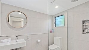 Een moderne badkamer met een ronde spiegel, een witte wastafel en toilet.