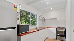Een moderne keuken met witte kasten, een roestvrijstalen koelkast, een magnetron, een spoelbak en een fornuis.