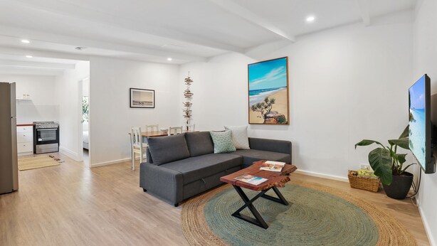 Een moderne woonkamer met een grijze modulaire bank, een houten salontafel en een groot schilderij van een strandgezicht.