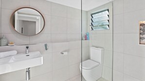 Un bany modern amb un lavabo blanc, un mirall rodó i una cabina de dutxa de vidre.