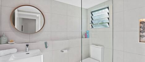 A modern bathroom with a white sink, mirror, and toilet.