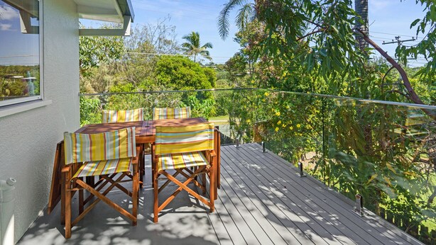 A wooden deck with a table and chairs, surrounded by lush greenery and palm trees. - 5 Unit Property - Lots of space and privacy for the whole group (Point Lookout)