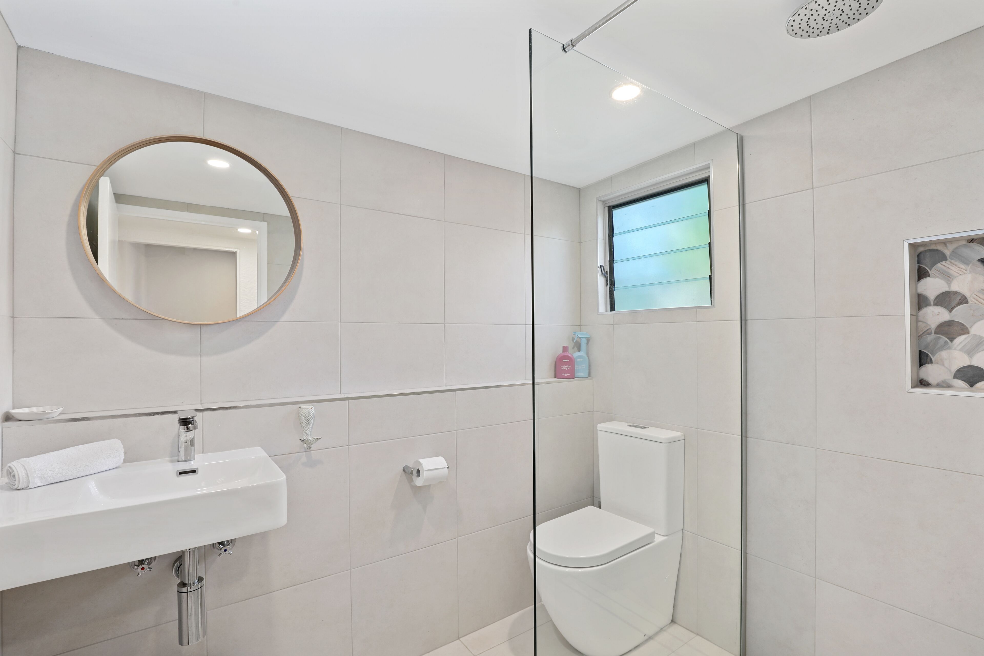 A modern bathroom with a round mirror, white sink, and toilet.