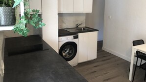 Et kompakt køkken med indbygget vaskemaskine og tørretumbler, en lille vask samt spiseplads med en stol.