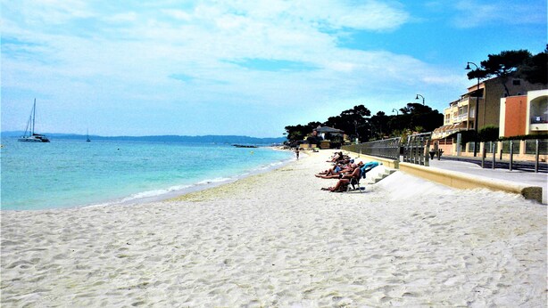 En strand med krystalklart turkis vand, en sandstrand og en række bygninger med altaner med udsigt over stranden.