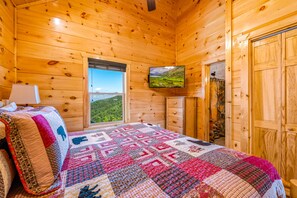 Una habitación de cabaña de madera con una cama, un televisor en la pared y una ventana con vistas a las montañas.