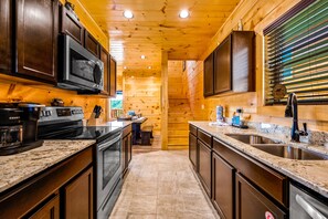 A modern kitchen with wooden walls, granite countertops, stainless steel appliances, and a built-in oven. - Free Attractions | Indoor Heated Pool, Game Room, Fireplace, Views (Sevierville)