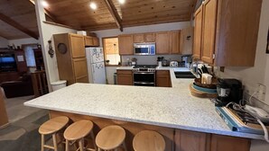 Eine Küche mit Holzausstattung, einer Granit Arbeitsplatte und einer Kochinsel mit Sitzgelegenheiten.