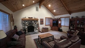 Ein gemütliches Wohnzimmer mit Kamin aus Stein, Ledersofas, einem Fernseher und einem Bücherregal.