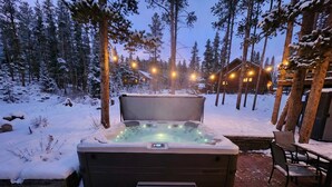 Un bain à remous installé dans un cadre extérieur enneigé, avec une terrasse en bois et des bancs.