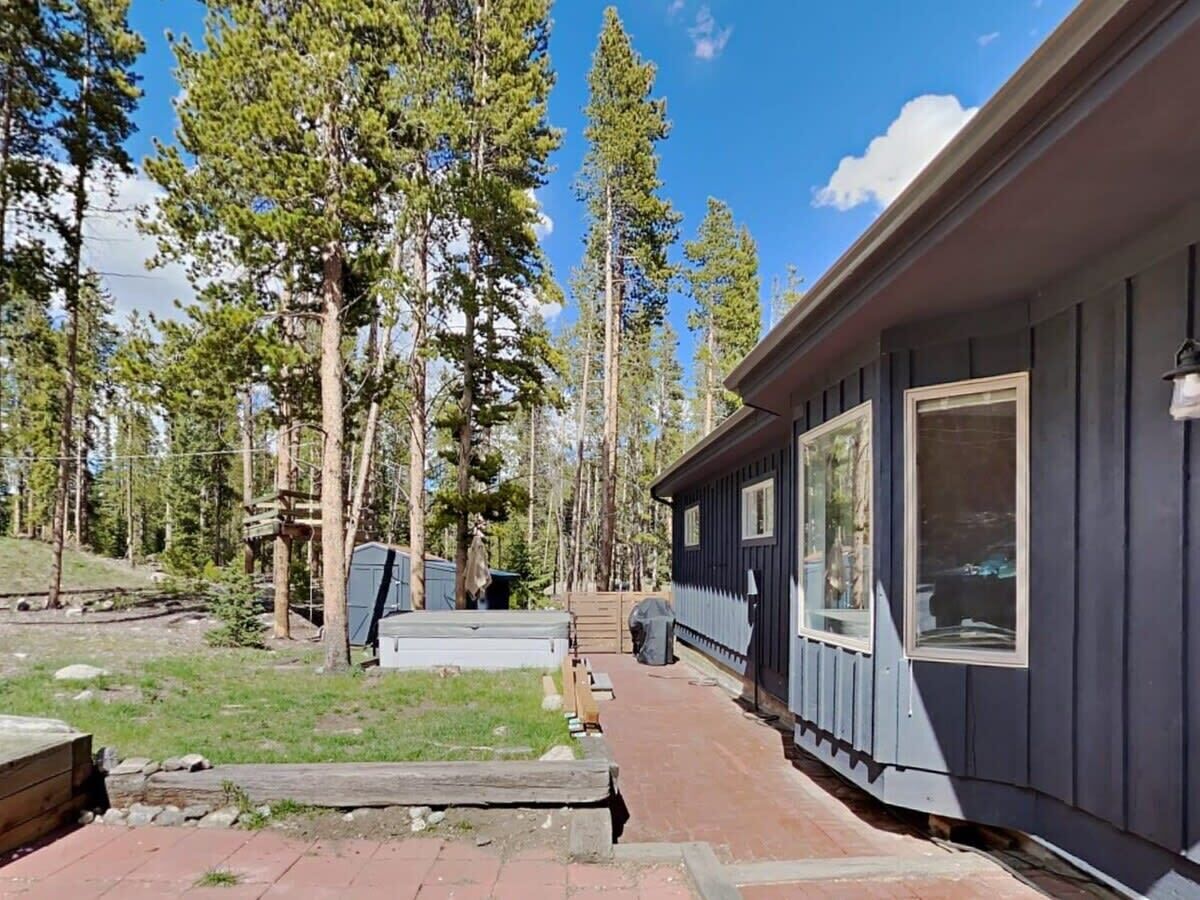 A cabin with a covered patio, surrounded by tall trees.