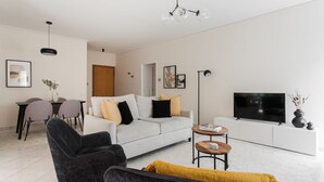 A modern living room with a sofa, a black armchair, a coffee table, and a television. - Top-Class 2BR Apartment in Marousi (Marousi)