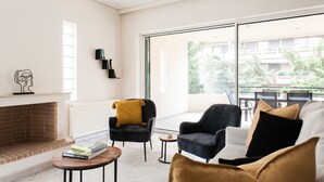 A modern living room with a fireplace, comfortable seating, and a large window offering a view of the outdoors. - Top-Class 2BR Apartment in Marousi (Marousi)
