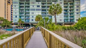 A multi-story hotel with balconies, a pool, and a wooden walkway leading to the entrance. - 🌟Oceanfront | Awesome Amenities | Great Views | Carolina Dunes 204🌟 (Myrtle Beach)