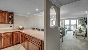 A spacious kitchen with wooden cabinets and a large island, leading to a dining area with a balcony. - 🌟Oceanfront | Awesome Amenities | Great Views | Carolina Dunes 204🌟 (Myrtle Beach)