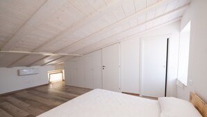 A bedroom with a wooden ceiling, a large bed, a wardrobe, and a window.