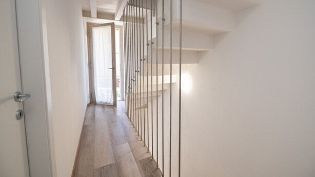 A modern interior with a wooden floor, white walls, and a metal railing along the stairs.
