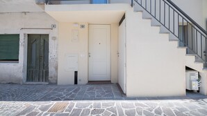 A building with a white door, a staircase with a metal railing, and a stone-paved ground.