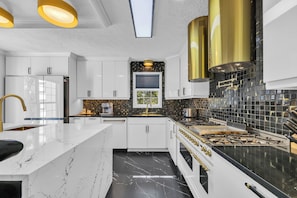 Una cocina moderna con armarios blancos, un salpicadero negro y dorado, y una isla central.