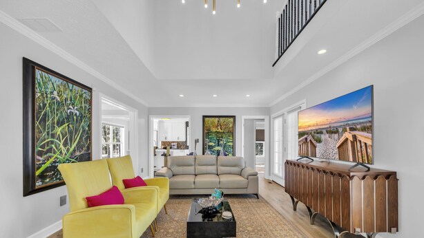 A spacious living room with a yellow sofa, a beige sofa, and a black coffee table. There are large paintings on the walls and a wooden console table.