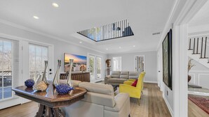 A spacious living area with a high ceiling, a dining table with decorative vases, a yellow armchair, and a sofa.