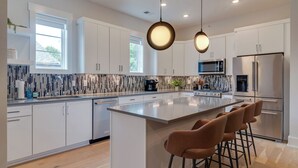 A modern kitchen with white cabinets, a central island with bar stools, a microwave, and a refrigerator. - Monthly West End Retreat In Elevator Building     |     3 King Beds, Patio, Spacious Long Term Listing, Sleeping Space for Guests, Perfect for Vanderbilt Students, Walk to Campus, 24 Hr Hospitality (Nashville)