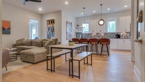 A modern living room with a sofa, a coffee table, and a dining area with chairs and a table. - Monthly West End Retreat In Elevator Building     |     3 King Beds, Patio, Spacious Long Term Listing, Sleeping Space for Guests, Perfect for Vanderbilt Students, Walk to Campus, 24 Hr Hospitality (Nashville)