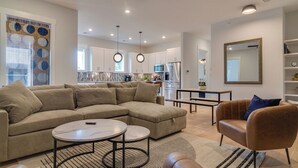 A modern living room with a sectional sofa, a round coffee table, and a leather armchair. - Monthly West End Retreat In Elevator Building     |     3 King Beds, Patio, Spacious Long Term Listing, Sleeping Space for Guests, Perfect for Vanderbilt Students, Walk to Campus, 24 Hr Hospitality (Nashville)