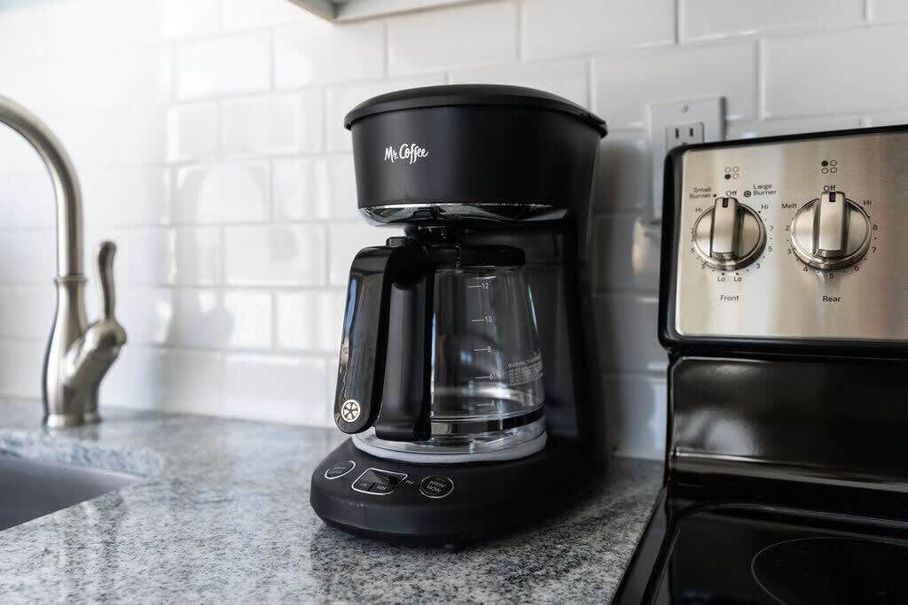 A black coffee maker with a clear carafe on a kitchen counter next to a stove with two knobs.