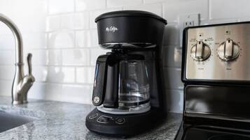 A black coffee maker with a clear carafe on a kitchen counter next to a stove with two knobs.