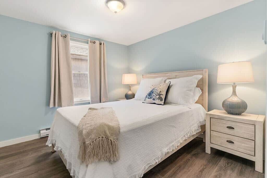 A bedroom with a bed, bedside lamps, a nightstand, and a window with curtains.