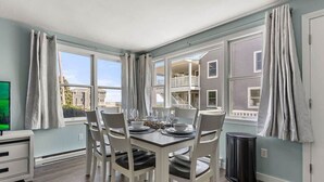 Un comedor con una mesa dispuesta para cuatro personas, ventanas amplias y vistas a edificios cercanos.