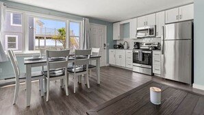 Una cocina moderna con armarios blancos, electrodomésticos de acero inoxidable y un comedor con mesa y sillas.