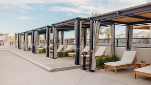Un área de lounge en la azotea con múltiples tumbonas y zonas de estar cubiertas, que ofrece vistas del paisaje circundante.