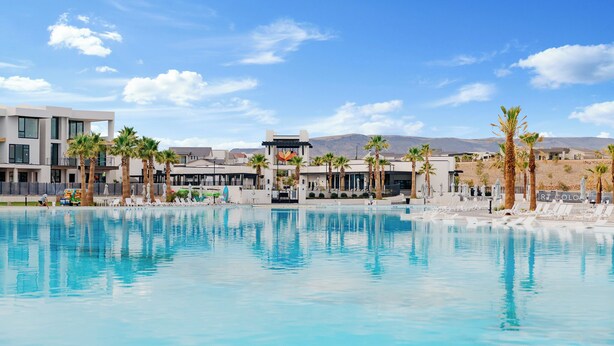 Un hotel moderno con piscina, palmeras y montañas al fondo.