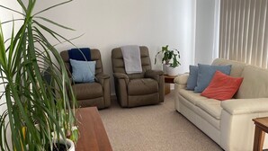A living room with a wooden coffee table, two recliner chairs, a beige sofa, and a potted plant. - Tyrone Beach Escape (Rye)