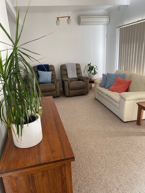 A living room with a wooden coffee table, two recliner chairs, a beige sofa, and a potted plant.